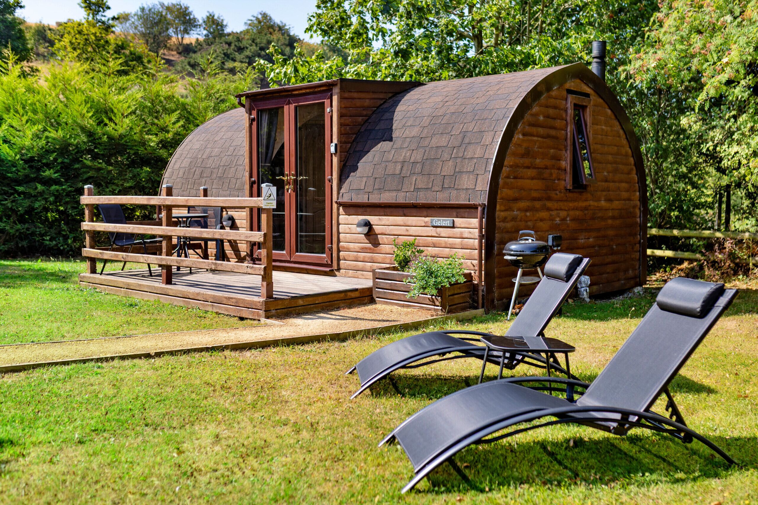 A wooden cabin with a curved roof, a deck with seating, and a barbecue area.