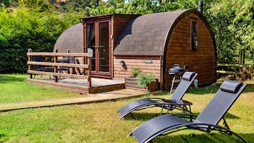 A wooden cabin with a curved roof, a deck with seating, and a barbecue area.