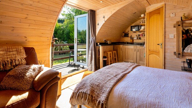 L’intérieur chaleureux d’un chalet avec un plafond en bois, un coin repas et une chambre dotée d’un grand lit.