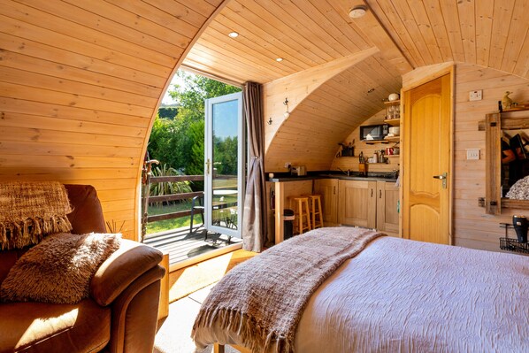 A cozy cabin interior with a wooden ceiling, a dining area, and a bedroom with a large bed.
