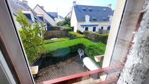 Ein Wohnhof mit gepflastertem Bereich, einem weißen Stuhl und einem kleinen Garten mit geschnittenen Hecken.