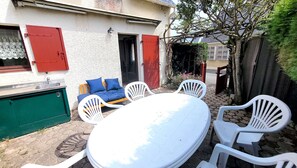An outdoor patio with a white table and chairs, a blue sofa with cushions, and a red door.