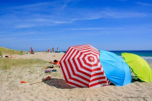 A beach with a red and white striped umbrella, a blue and green tent, and people relaxing on the sand.