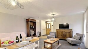 A modern living room with a dining area, a television, and a wooden cabinet. - Cottage 'Gîte Le Lac Du Vert' with Lake View, Wi-Fi and Air Conditioning (Cheminas)
