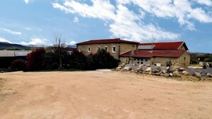 A two-story stone building with a red roof, surrounded by a dirt path and sparse vegetation. - Cottage 'Gîte Le Lac Du Vert' with Lake View, Wi-Fi and Air Conditioning (Cheminas)