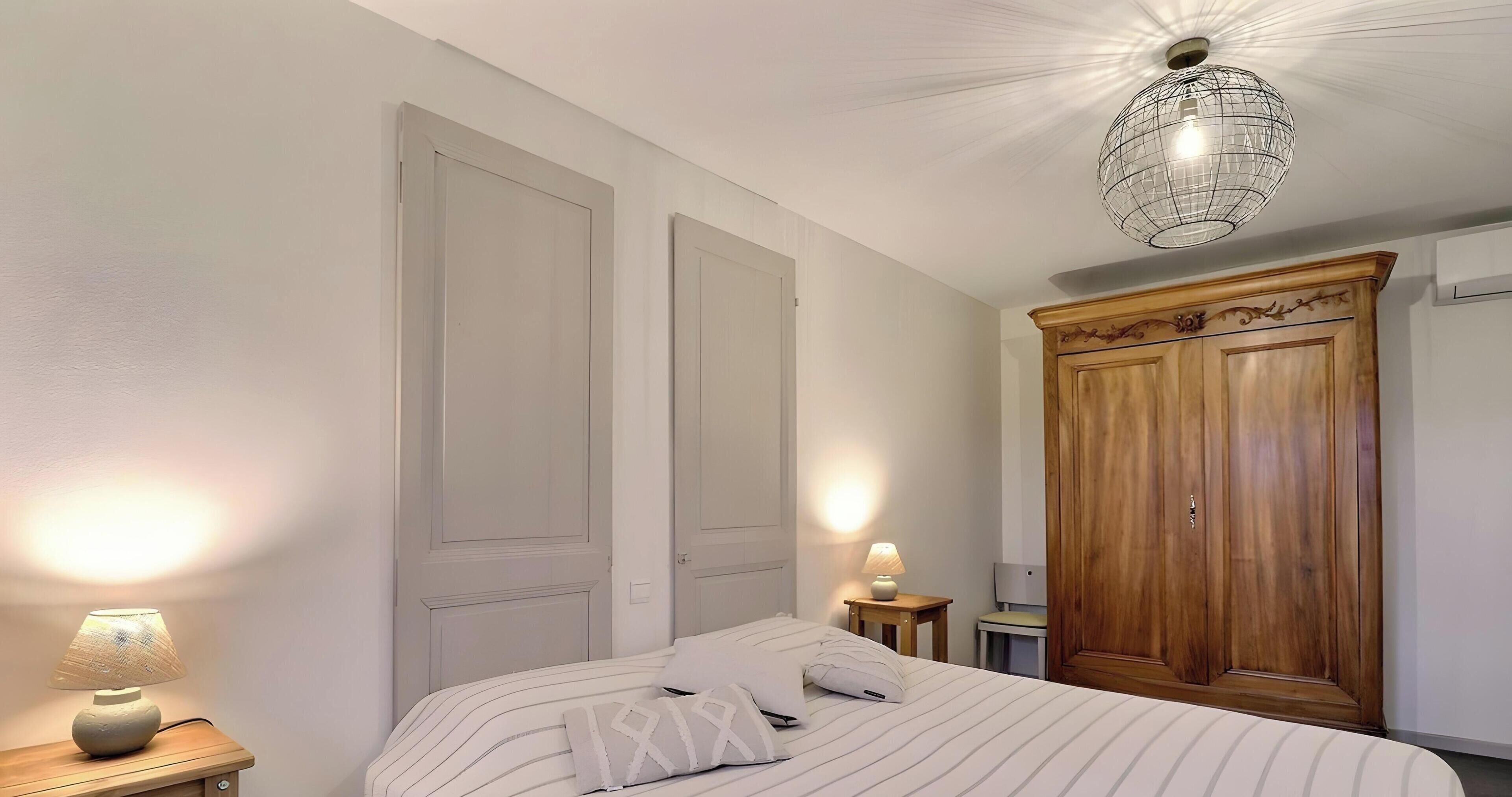Une chambre à coucher avec un lit, des lampes de chevet, une armoire en bois et un luminaire suspendu.