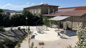 A patio area with outdoor furniture, a covered seating area, and a stone building with a tiled roof. - Cottage 'Gîte Le Lac Du Vert' with Lake View, Wi-Fi and Air Conditioning (Cheminas)
