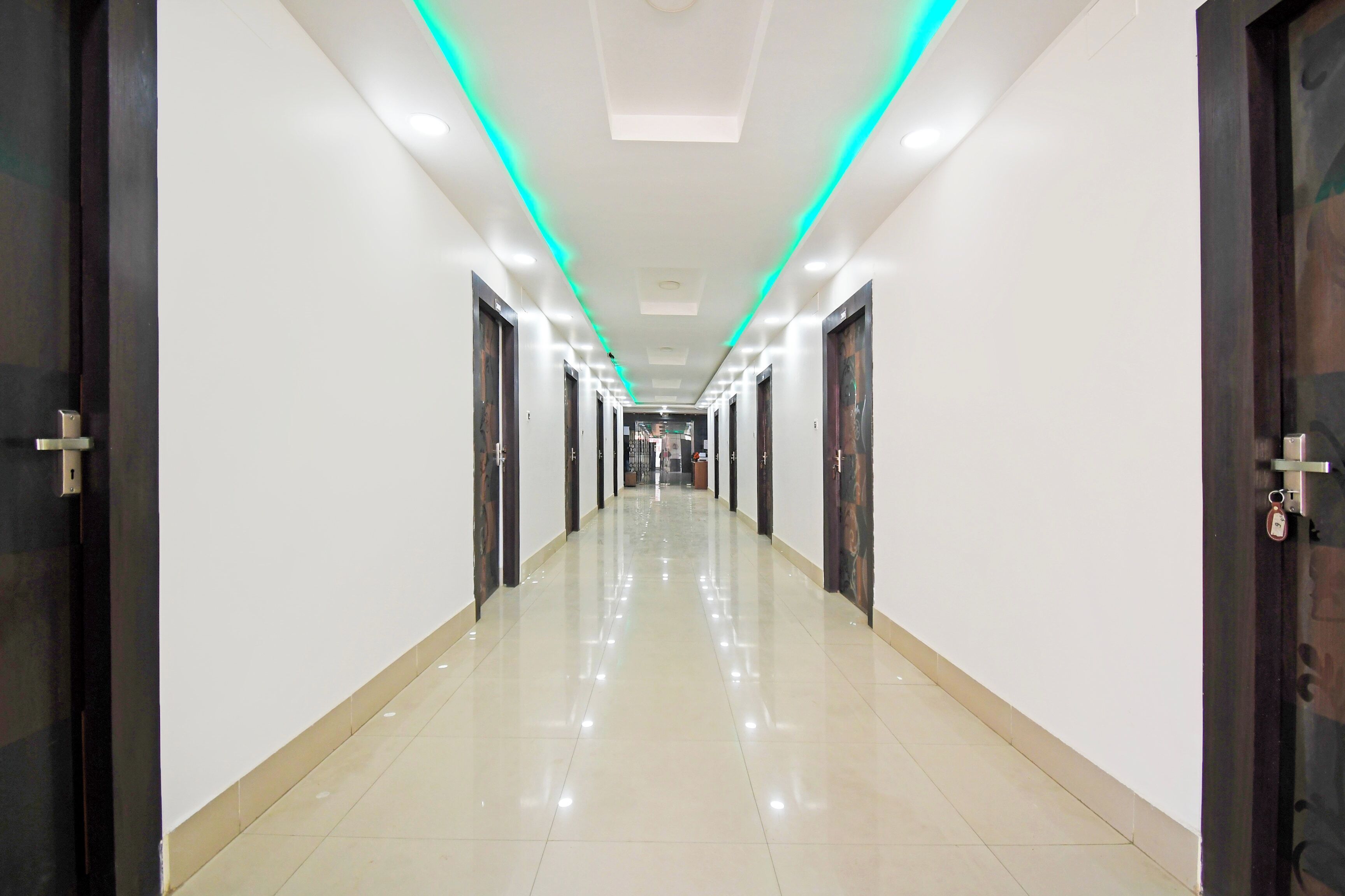 Un pasillo largo e iluminado con puertas a ambos lados, que conduce a un área central con una lámpara en el techo.