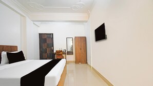 Quarto de hotel com cama, guarda-roupa de madeira, secretária com cadeira, televisão de tela plana na parede e espelho.