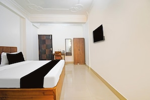 A hotel room with a bed, a wooden wardrobe, a desk with a chair, a flat-screen TV mounted on the wall, and a mirror on the wall. - Super Collection O Raja Bazar Bailey (Patna)