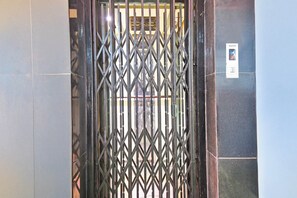 A metal gate with a diamond pattern, a wall-mounted elevator control panel, and a tiled wall. - Super Collection O Raja Bazar Bailey (Patna)