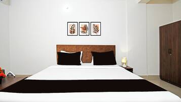 A hotel room with a large bed, a wooden headboard, a nightstand with a lamp, and three framed artworks on the wall.