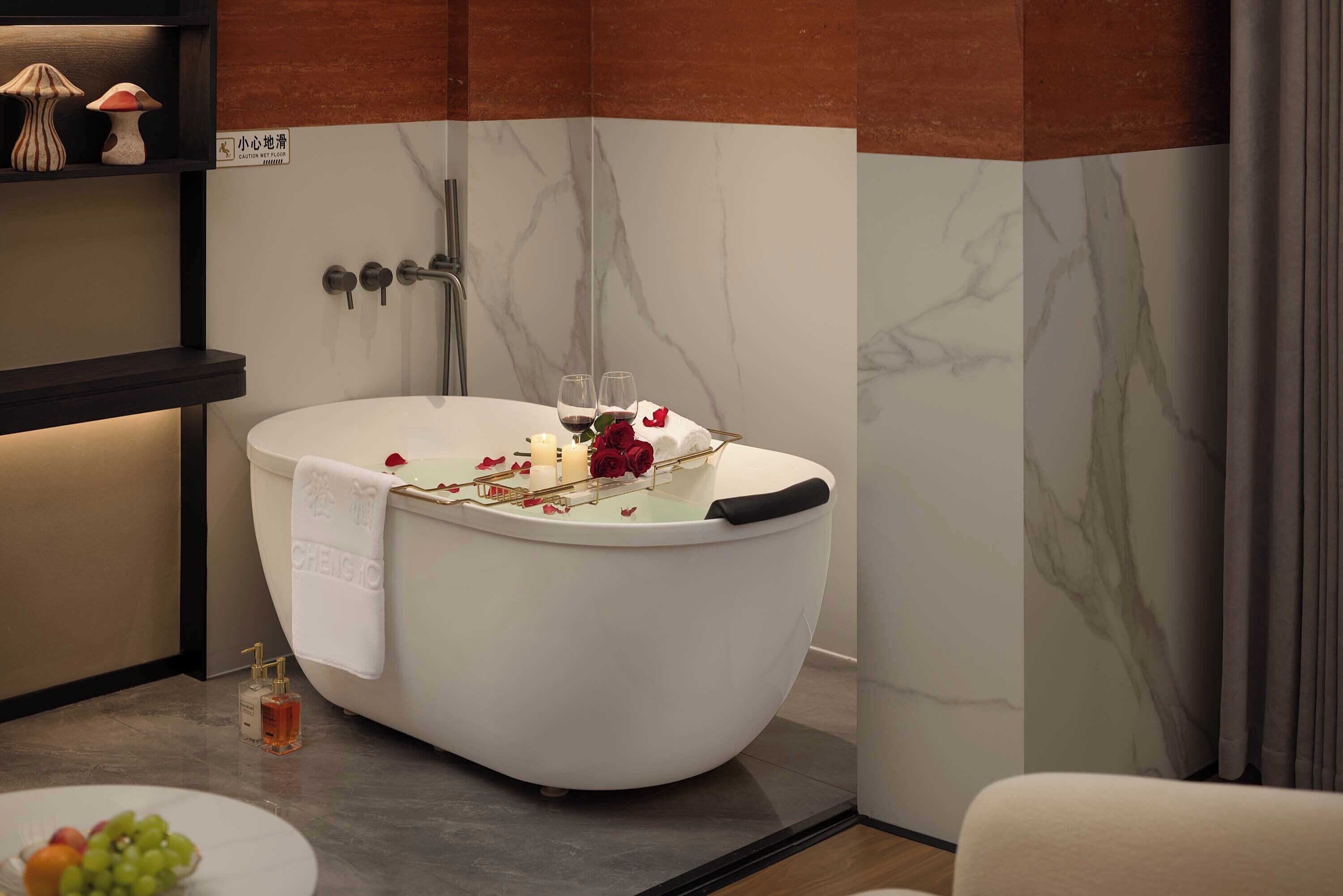 A modern bathroom with a freestanding bathtub, a towel rack, a glass of wine, and rose petals.