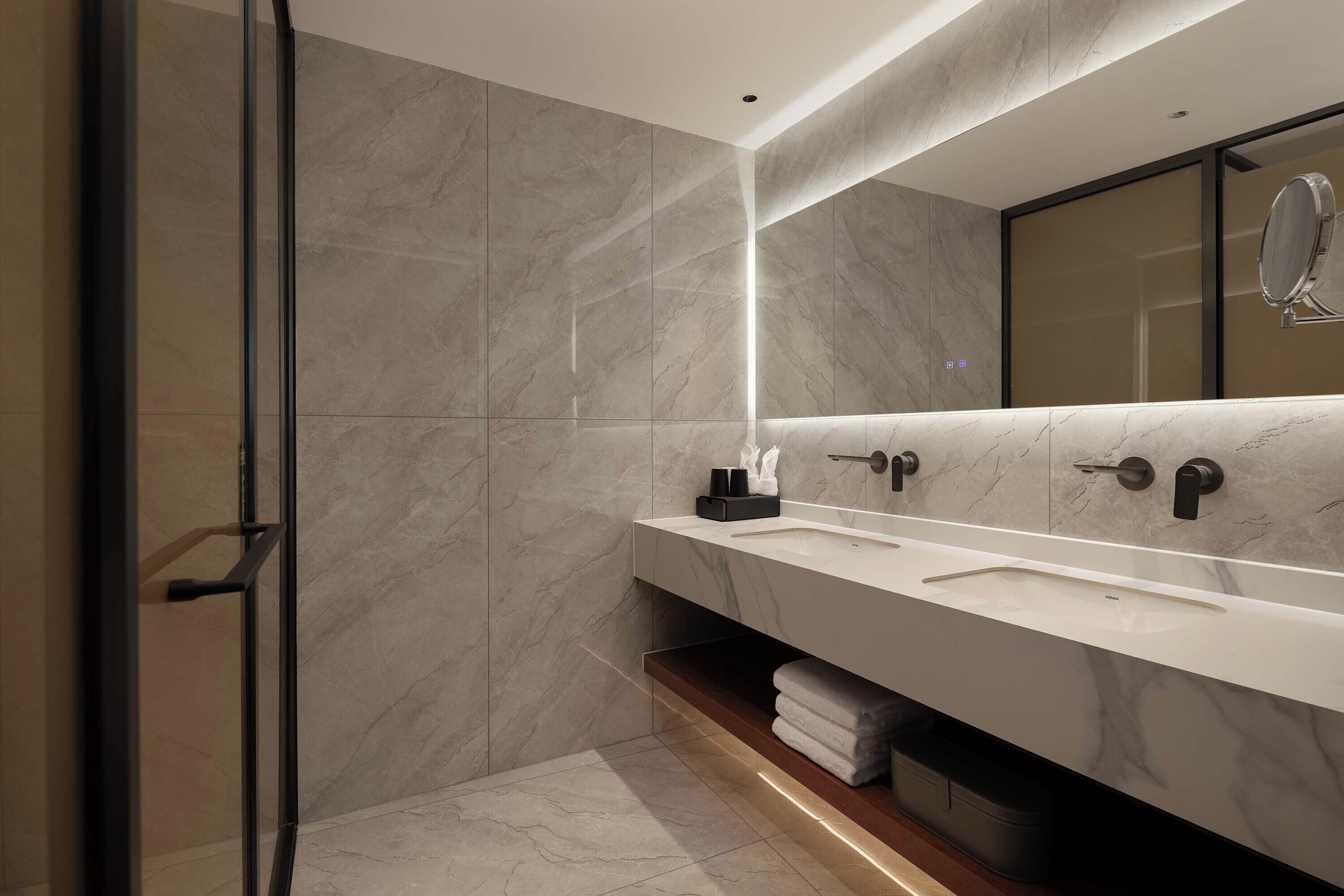 A modern bathroom with a glass shower door, a large mirror, and a vanity with a sink and towel storage.
