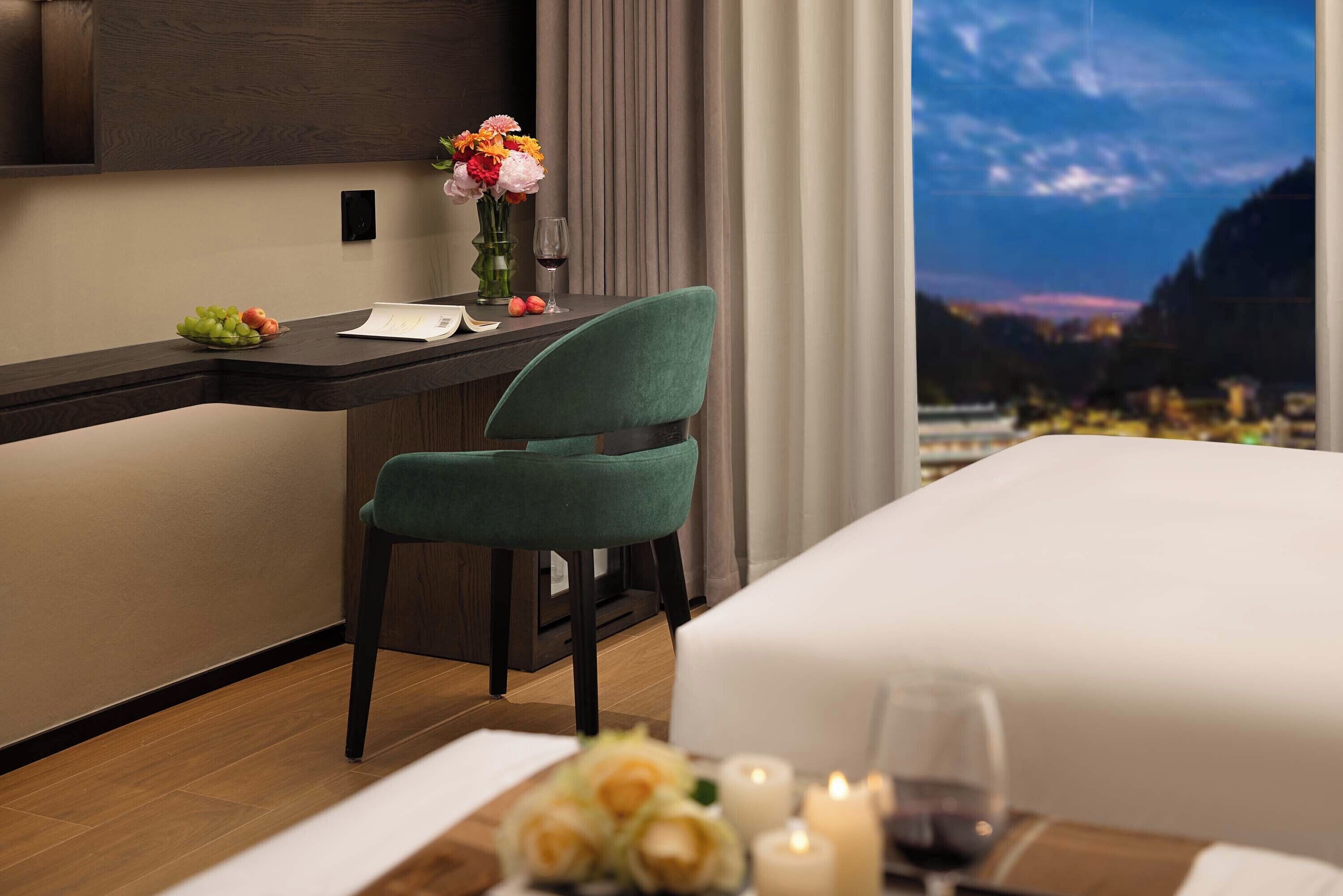 A hotel room with a bed, a desk, a chair, a view of the mountains, and a night sky.