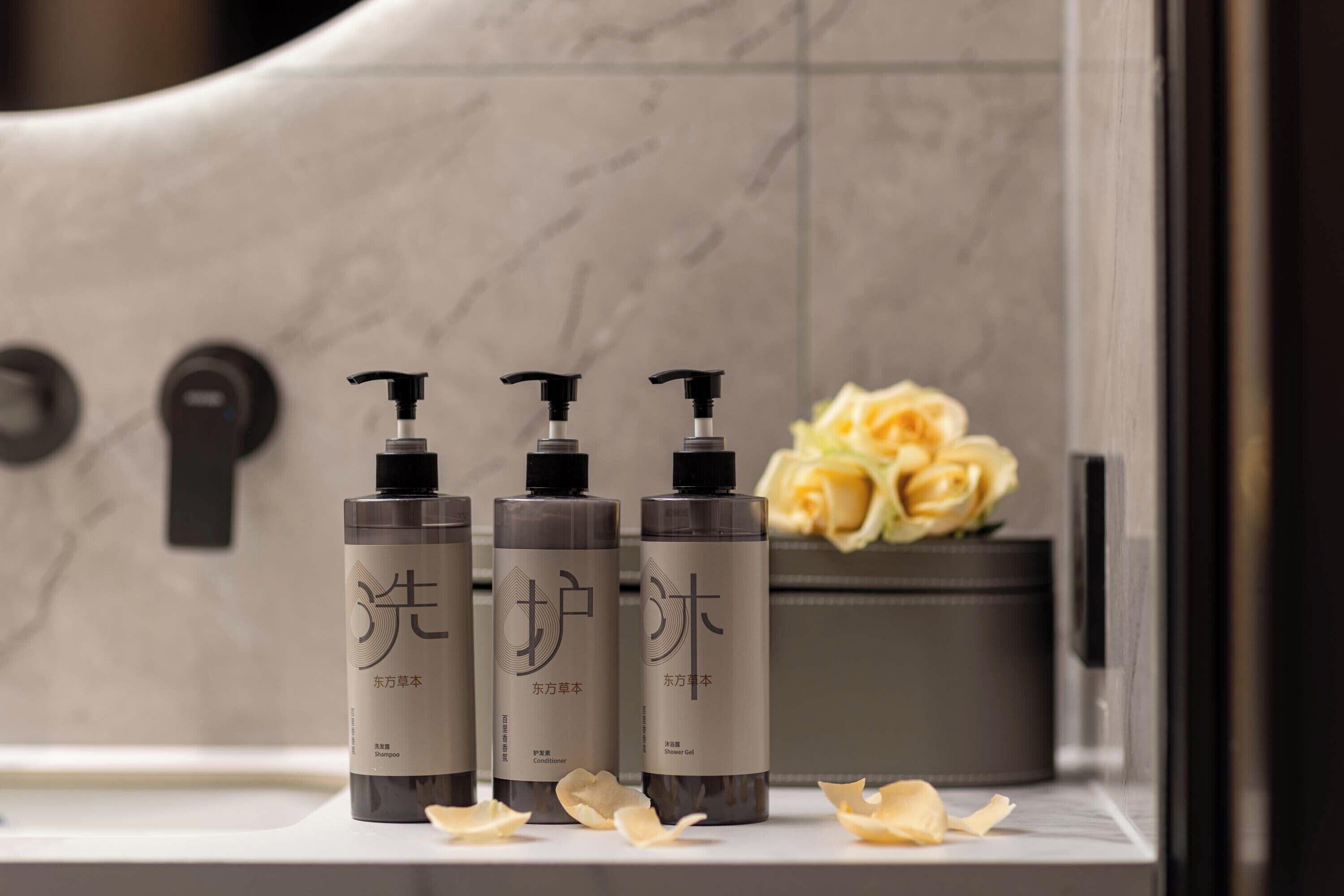 Tre flaconi di shampoo, balsamo e gel doccia su un ripiano del bagno, con una serratura e un vaso di fiori.