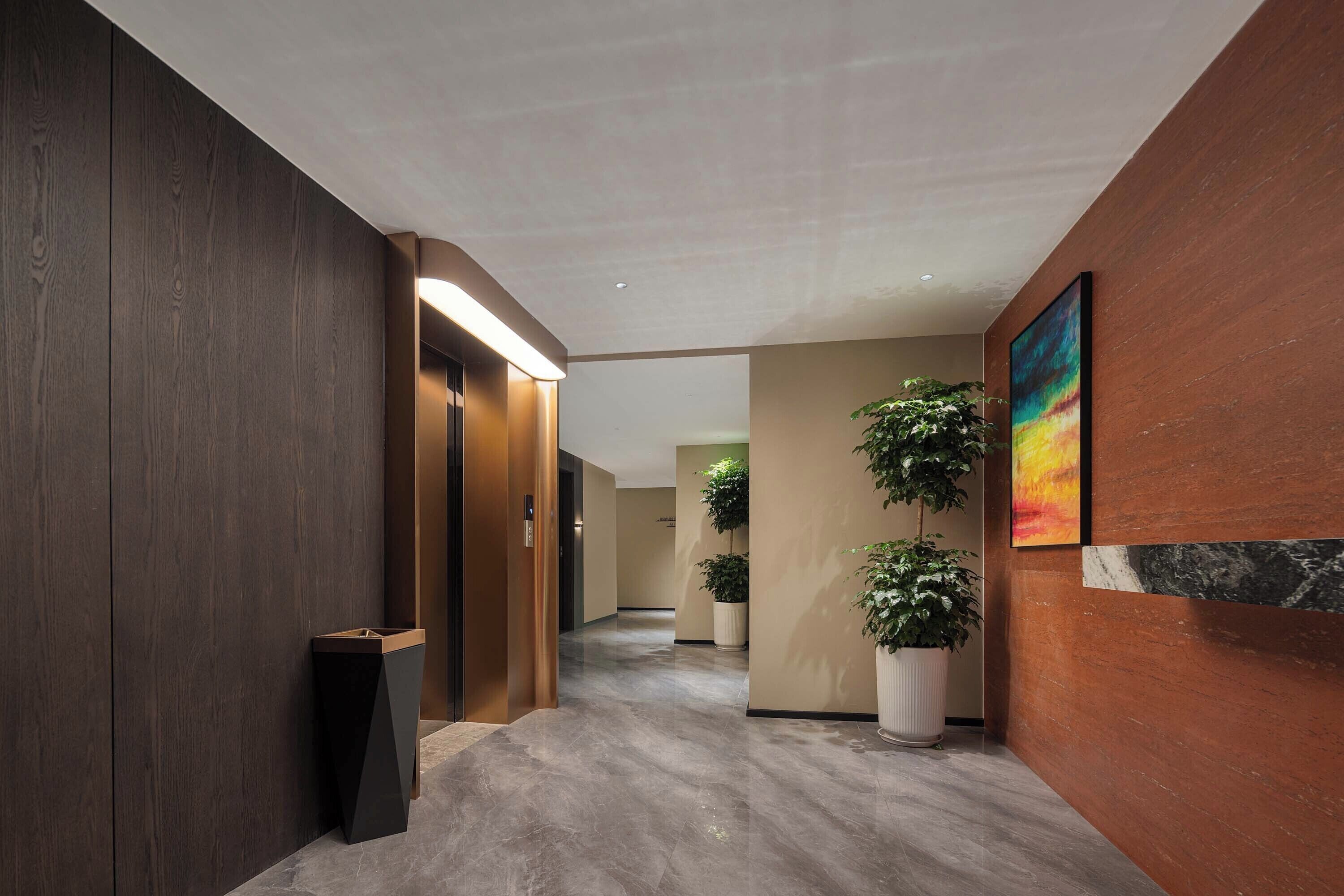 A modern hallway with a wooden wall, a trash bin, a potted plant, and a painting.