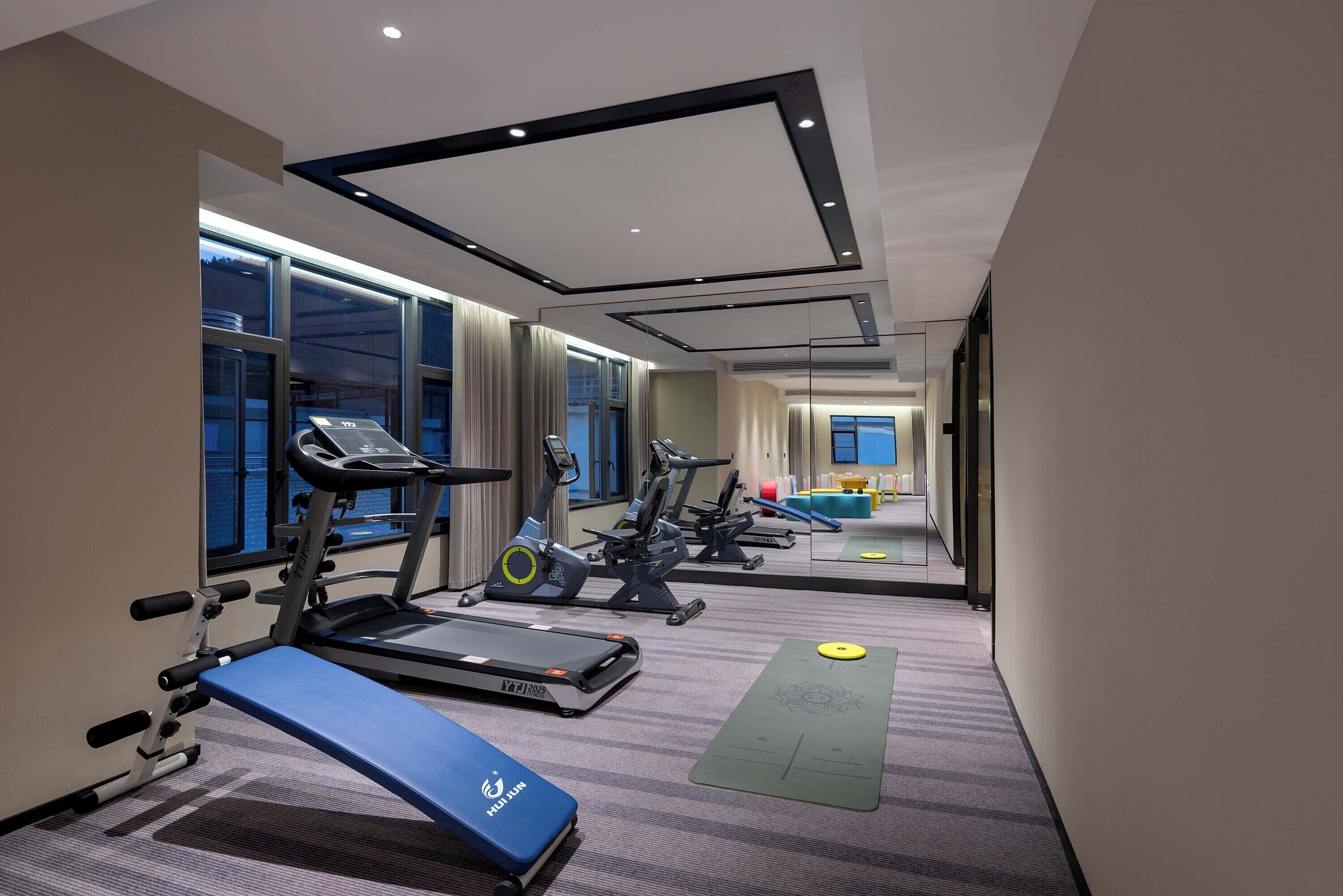 Een sportschool met loopbanden, hometrainers en een yogamat.