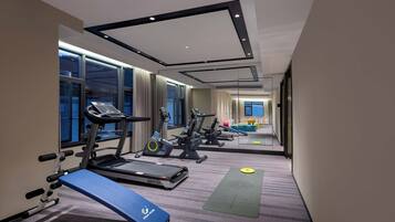 Een sportschool met loopbanden, hometrainers en een yogamat.