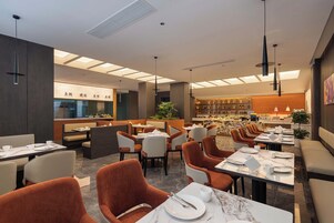 Um restaurante moderno com um bar central, várias mesas de jantar com cadeiras e um teto com claraboias.