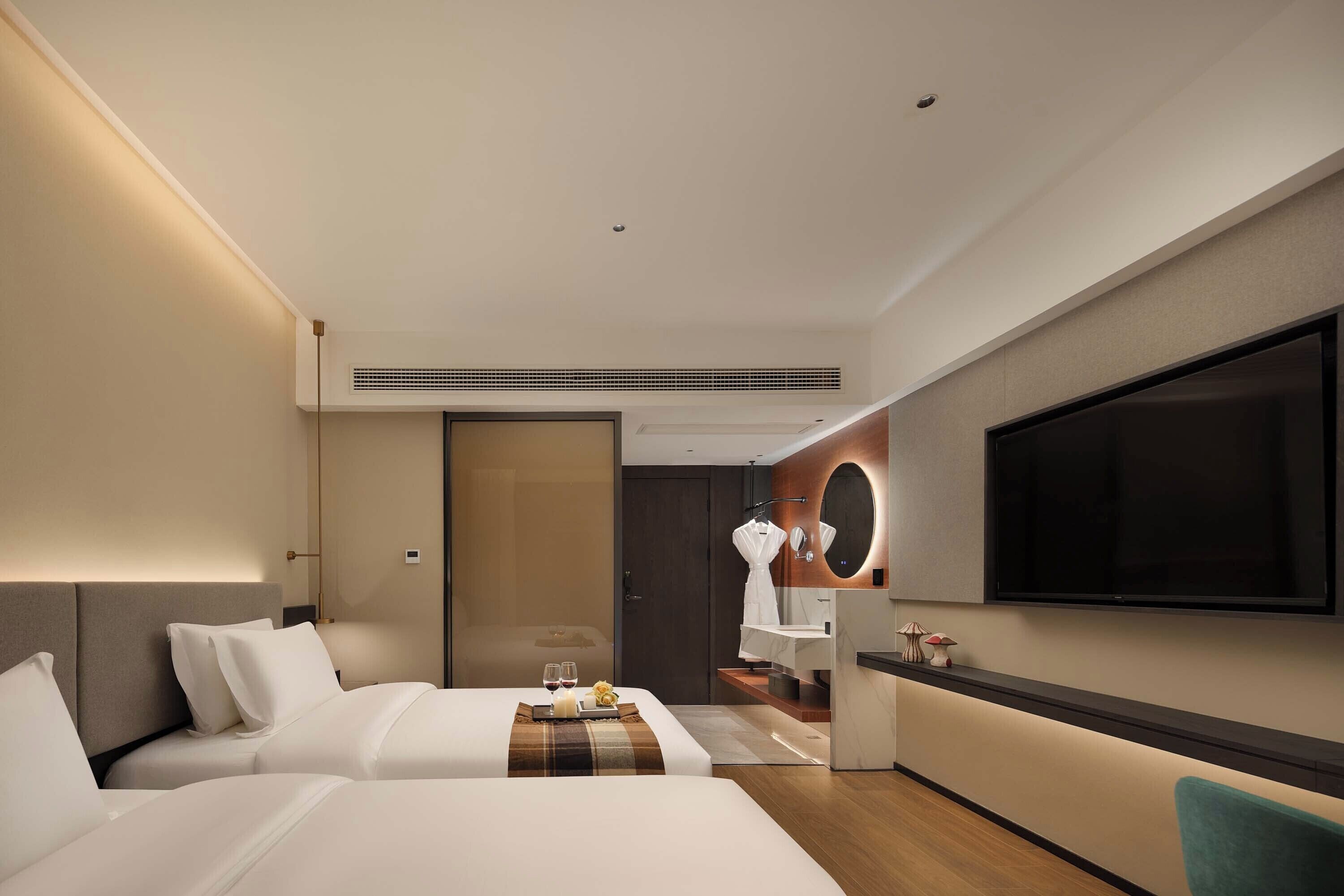 Camera d'albergo con un letto, comodino, televisione e bagno con specchio e lavandino.