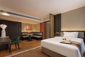 Quarto de hotel com cama, área de estar, escrivaninha e um porta-robes.