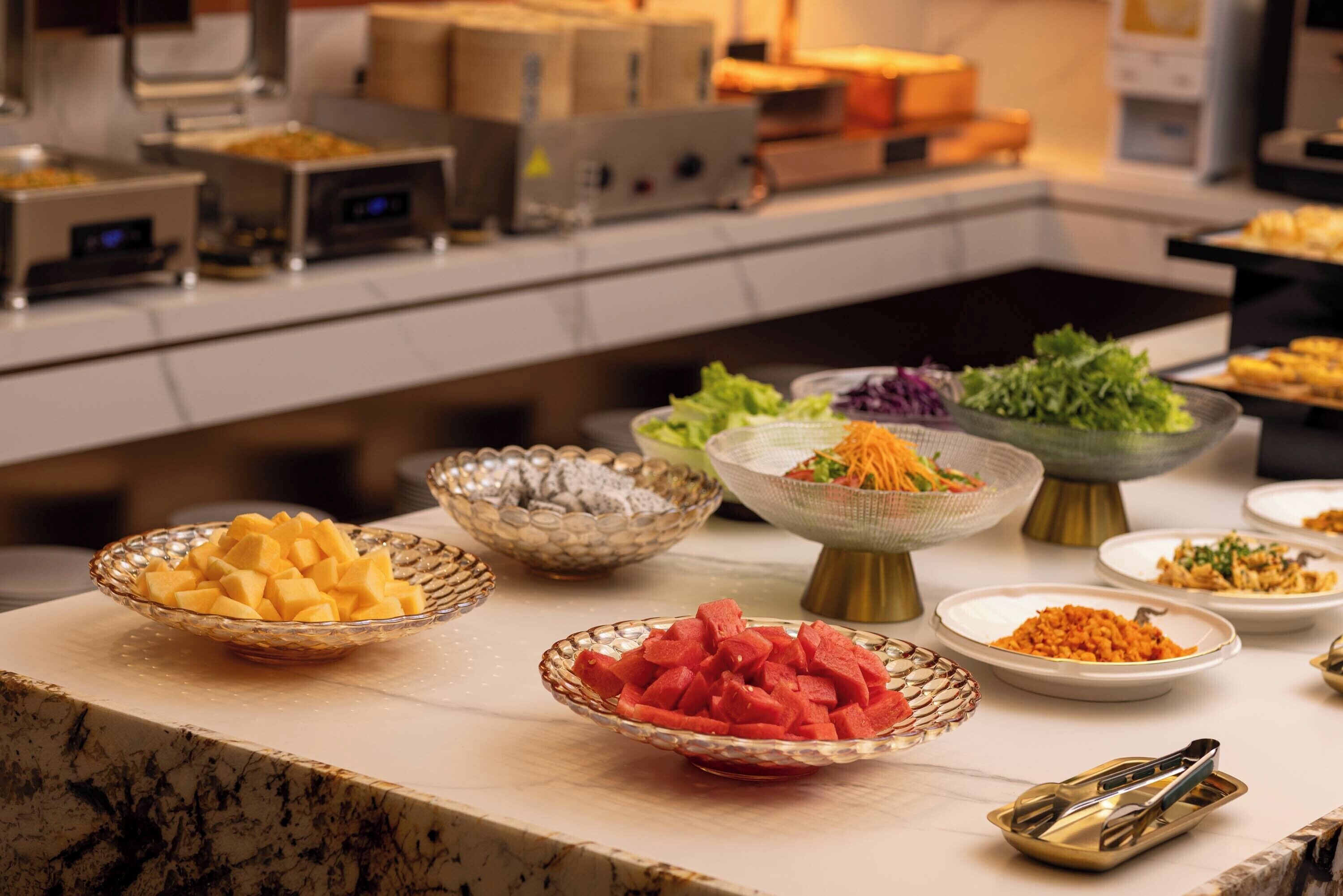 Une table de buffet proposant divers plats, notamment des fruits et des salades.