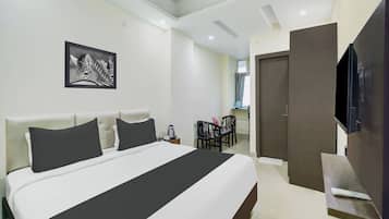 Una habitación de hotel con una cama grande, un televisor de pantalla plana, una zona de comedor con sillas y una puerta que da a otra habitación.