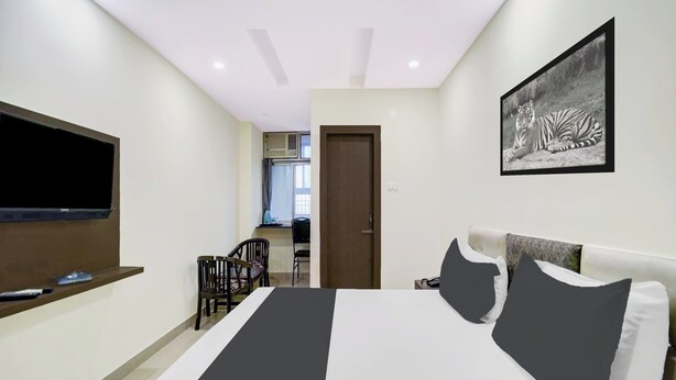 A hotel room with a bed, a TV mounted on the wall, a painting, and a kitchenette in the background. - Collection O Rajeev Nagar Near Atal Path (Patna)