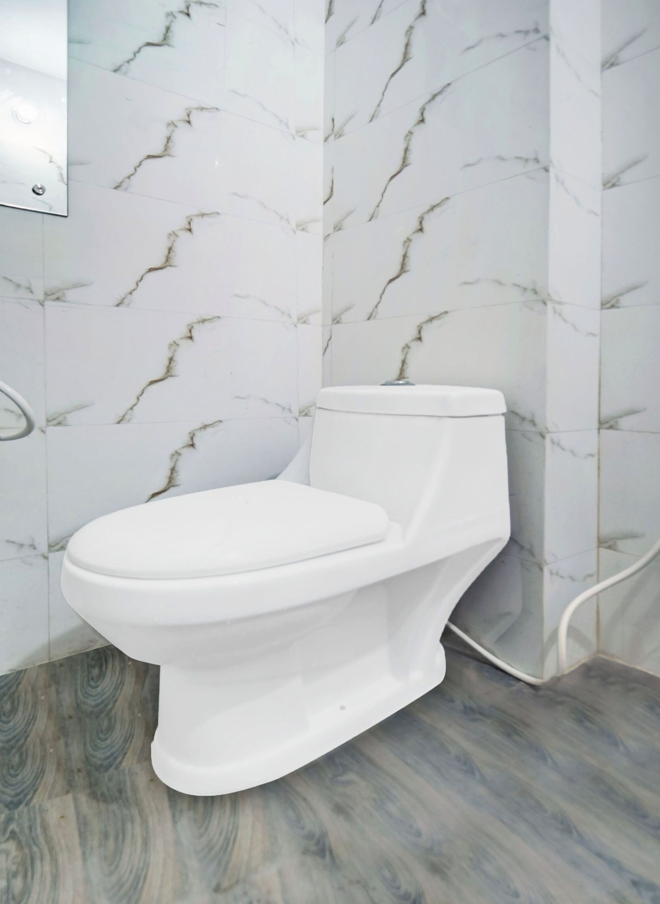 A toilet in a bathroom with marble-patterned walls and a wooden floor.