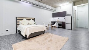 A modern bedroom with a bed, bedside tables, a desk, and a kitchenette.