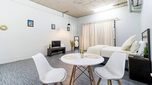 A modern living room with a sofa, two white chairs, a TV, and a small table with decorative items.