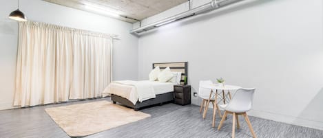 A modern bedroom with a bed, bedside table, and a small white table with chairs.