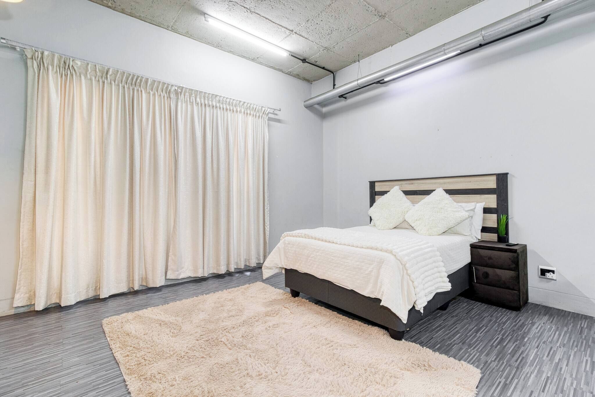 A bedroom with a bed, nightstand, and a large window with curtains.