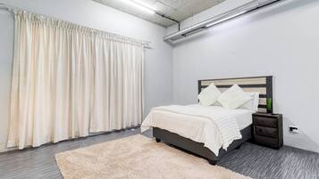 A bedroom with a bed, nightstand, and a large window with curtains.