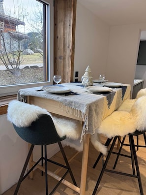 A dining area with a table set for two, a view of the outdoors through a window, and a wooden post in the background. - The Courchevel Nests: LA LOGE, Le Praz (Courchevel)