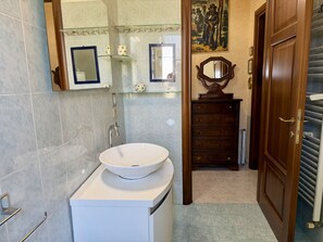 Une salle de bain avec un lavabo blanc, un meuble en bois, un miroir et une porte.