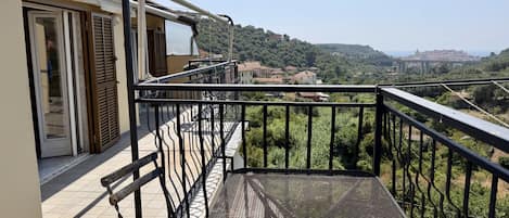 A balcony with a metal railing overlooking a residential area with houses and a distant bridge.
