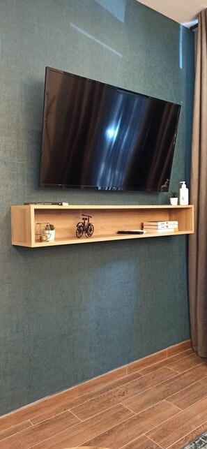 A flat-screen TV mounted on a wall above a wooden shelf with a bicycle, books, and a small plant. - A magnificent, brand-new house next to Plaza España (Valencia)
