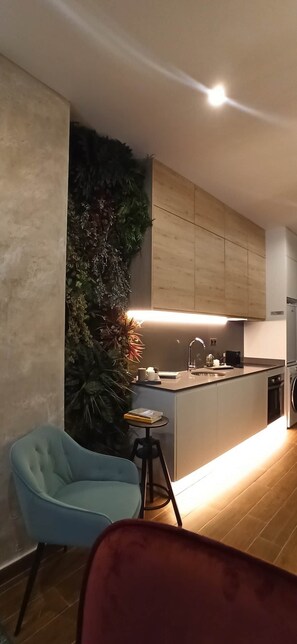 A modern kitchen with wooden cabinets, a built-in island, and a decorative wall with foliage. There is a blue chair and a red chair in the foreground. - A magnificent, brand-new house next to Plaza España (Valencia)