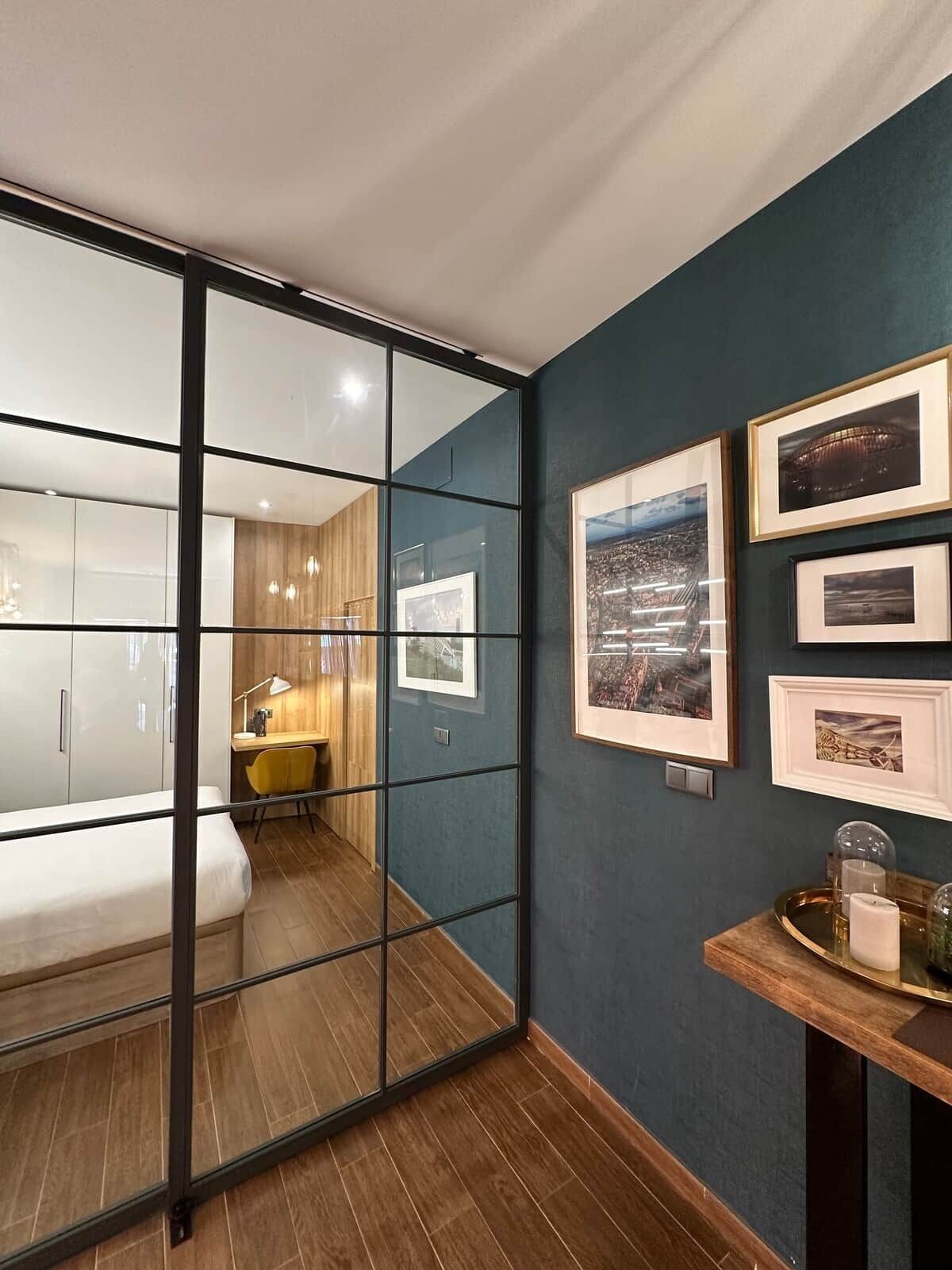 Een moderne slaapkamer met glazen wand, houten vloer, een bed, bureau en wanddecoratie.