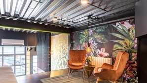 A modern interior with a tropical mural, two upholstered chairs, a patterned rug, and a ceiling with exposed beams. - To complete (Valencia)