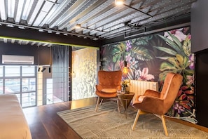 A modern interior with a tropical mural, two upholstered chairs, a patterned rug, and a ceiling with exposed beams. - To complete (Valencia)