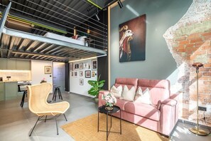 A modern living space with a loft area, a pink sofa, a wicker chair, and a large artwork on the wall. - To complete (Valencia)