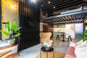 A modern interior with a flat-screen TV mounted on a black wall, a wicker chair, a round table with a vase of flowers, and a pink sofa. - To complete (Valencia)