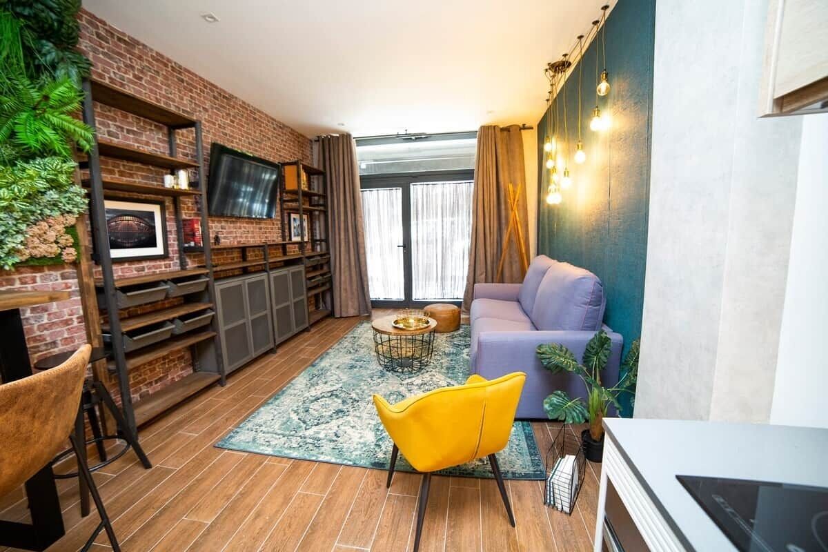 Un salon avec un mur en briques, un téléviseur, un canapé, un fauteuil jaune et une table basse.