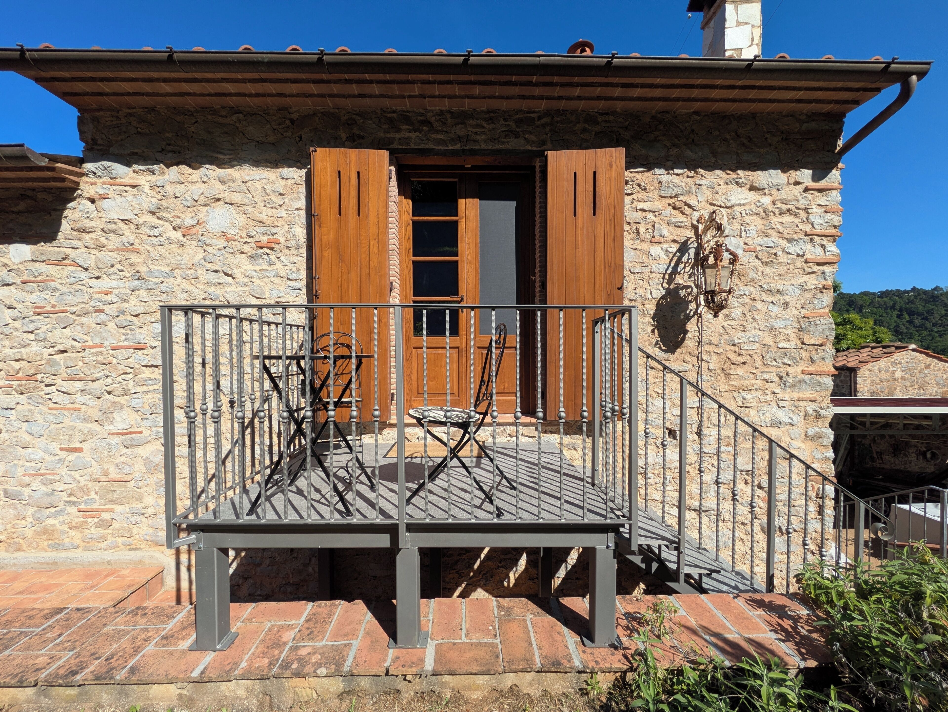 A stone building with a balcony, wooden shutters, and a metal railing.