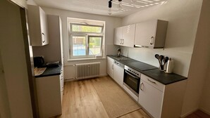 Een moderne keuken met witte kasten, een zwart aanrecht en een raam met jaloezieën.