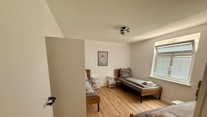 Een kleine slaapkamer met een enkel bed, een nachtkastje, een stoel en een raam met zonwering.