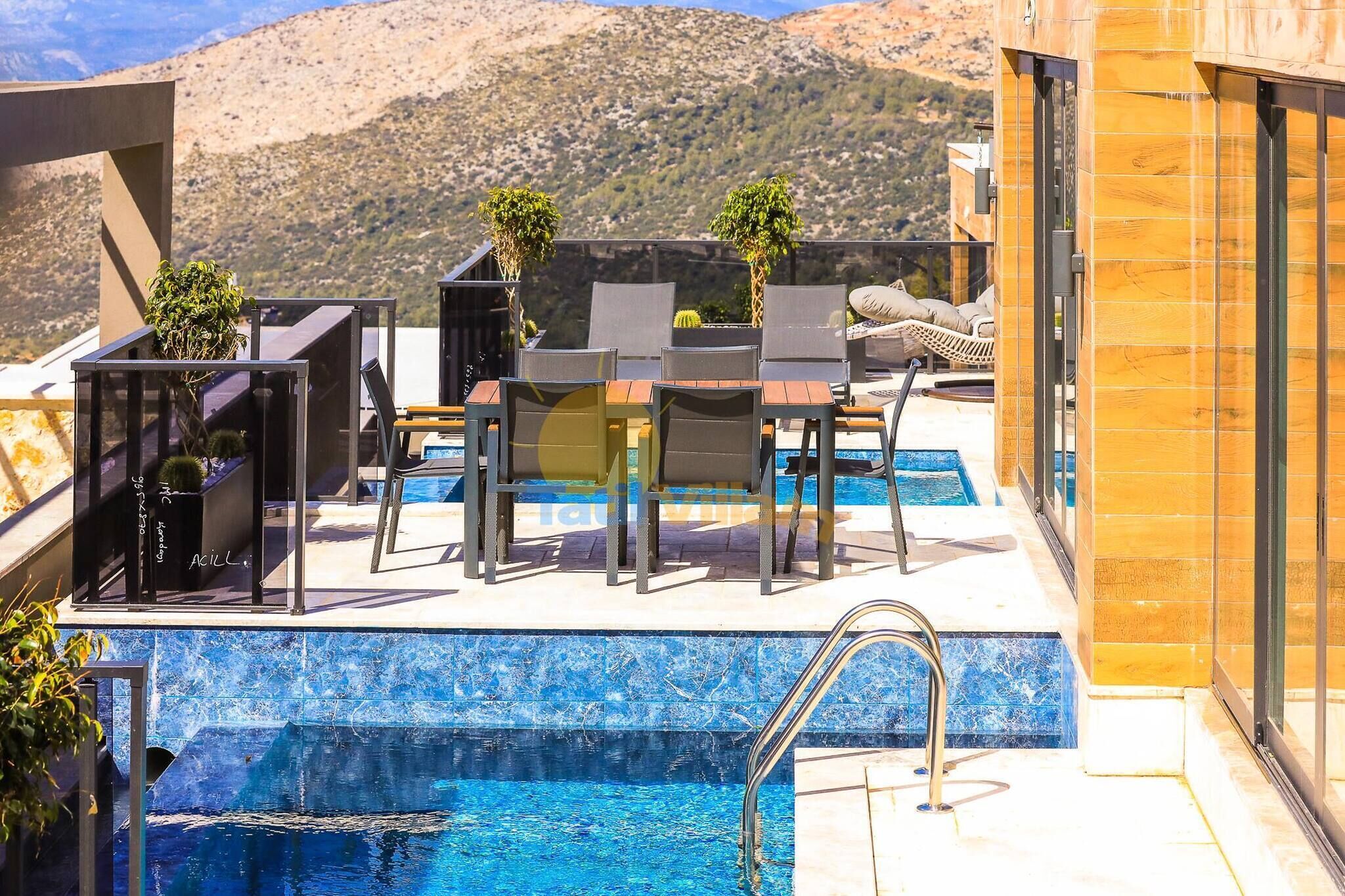 A rooftop pool area with a view of mountains, including a table and chairs, and a small garden.